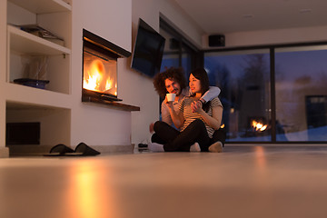 Image showing happy multiethnic couple sitting in front of fireplace