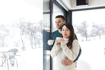 Image showing multiethnic couple enjoying morning coffee by the window