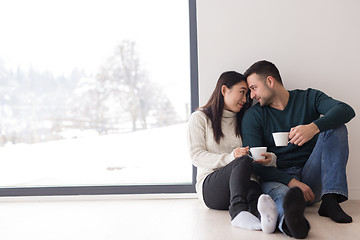 Image showing multiethnic couple enjoying morning coffee by the window