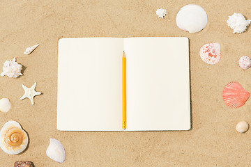 Image showing notebook with pencil and seashells on beach sand