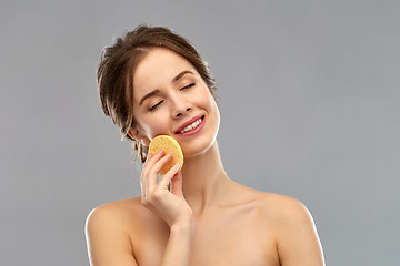 Image showing young woman cleaning face with exfoliating sponge