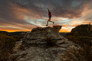 Image showing Active woman jumping on mountain cliffs at sunset