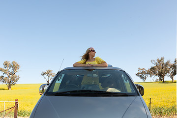 Image showing Beautiful woman standing in the sunroof of her car on a road trip to countryside