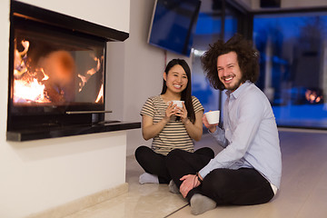 Image showing happy multiethnic couple sitting in front of fireplace