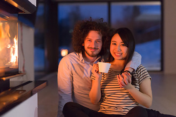 Image showing happy multiethnic couple sitting in front of fireplace