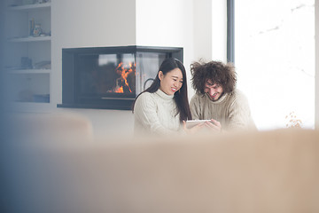 Image showing multiethnic couple using tablet computer in front of fireplace