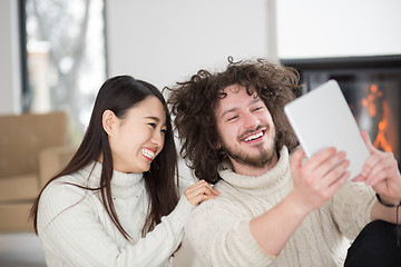 Image showing multiethnic couple using tablet computer in front of fireplace