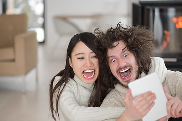 Image showing multiethnic couple using tablet computer in front of fireplace