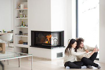 Image showing multiethnic couple using tablet computer in front of fireplace