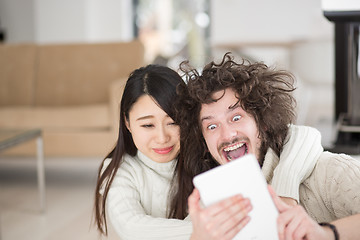 Image showing multiethnic couple using tablet computer in front of fireplace