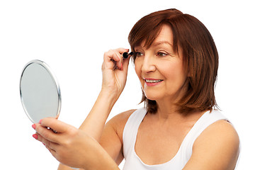 Image showing smiling senior woman with mirror applying mascara