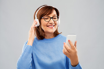 Image showing senior woman in headphones listening music on cell