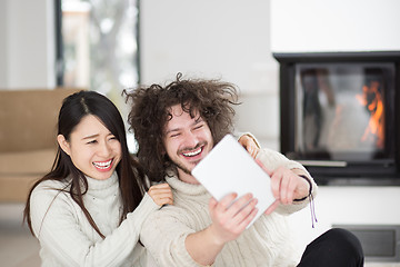 Image showing multiethnic couple using tablet computer in front of fireplace