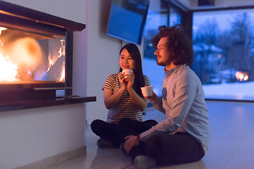 Image showing happy multiethnic couple sitting in front of fireplace