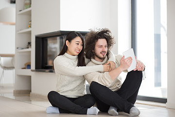 Image showing multiethnic couple using tablet computer in front of fireplace