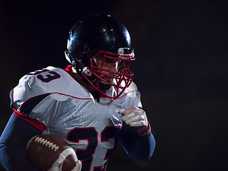 Image showing American football player holding ball while running on field