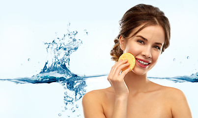 Image showing young woman cleaning face with exfoliating sponge