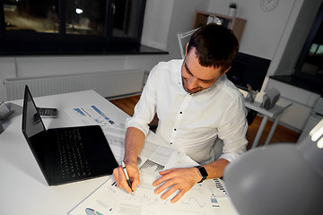 Image showing businessman with papers and laptop at night office