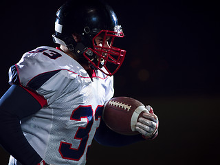 Image showing American football player holding ball while running on field