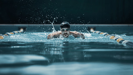 Image showing dynamic and fit swimmer in cap breathing performing the butterfly stroke