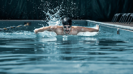 Image showing dynamic and fit swimmer in cap breathing performing the butterfly stroke