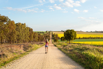 Image showing Woman walking along a dusty road among the rural fields