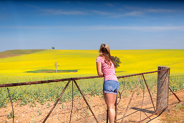 Image showing Female leaning on farm gate looks over rolling hills farmlands of golden canola