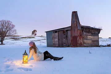 Image showing Woman with lantern sitting in a snow covered field