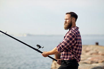 Image showing bearded fisherman with fishing rod on pier at sea