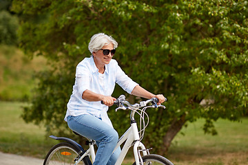 Image showing happy senior woman riding bicycle at summer park