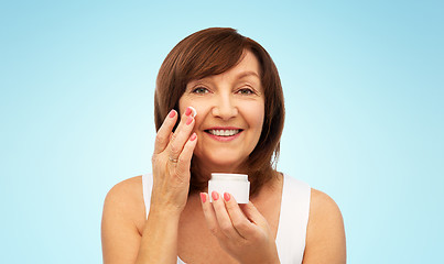Image showing smiling senior woman applying cream to her face