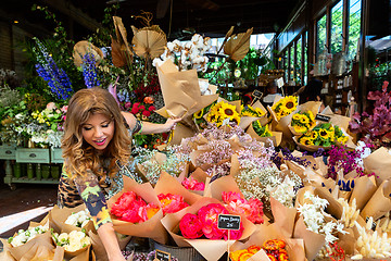 Image showing Woman on footpath choosing bunches of flowers from florist