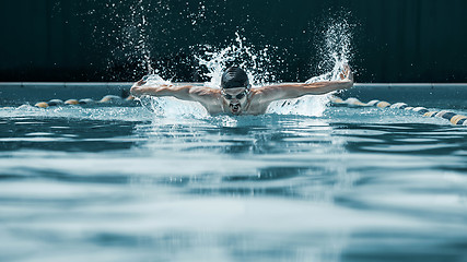 Image showing dynamic and fit swimmer in cap breathing performing the butterfly stroke