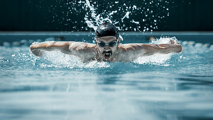 Image showing dynamic and fit swimmer in cap breathing performing the butterfly stroke