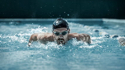 Image showing dynamic and fit swimmer in cap breathing performing the butterfly stroke