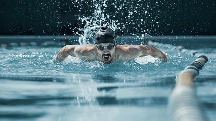 Image showing dynamic and fit swimmer in cap breathing performing the butterfly stroke