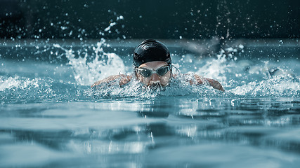 Image showing dynamic and fit swimmer in cap breathing performing the butterfly stroke