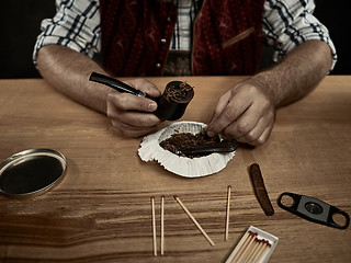 Image showing bearded man clogs the tobacco in pipe