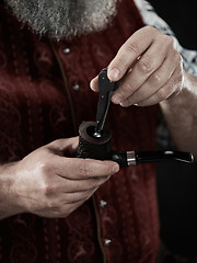 Image showing bearded man clogs the tobacco in pipe