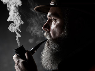 Image showing Black and white dramatic portrait of senior smoking tobacco pipe