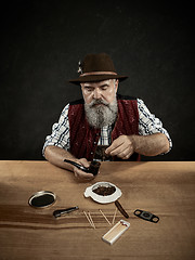 Image showing bearded man clogs the tobacco in pipe