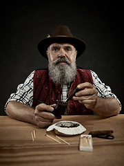 Image showing bearded man clogs the tobacco in pipe