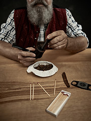 Image showing bearded man clogs the tobacco in pipe