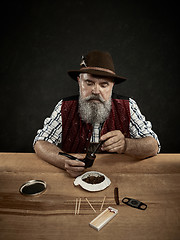 Image showing bearded man clogs the tobacco in pipe