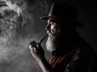 Image showing Black and white dramatic portrait of senior smoking tobacco pipe