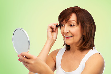 Image showing smiling senior woman with mirror applying mascara