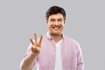 Image showing young man showing three fingers over grey