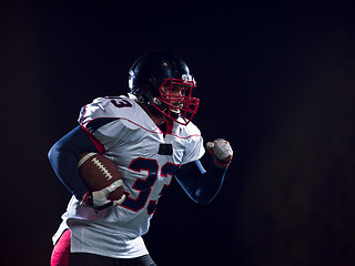 Image showing American football player holding ball while running on field