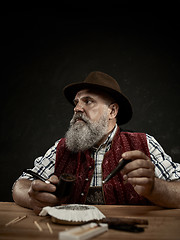 Image showing bearded man clogs the tobacco in pipe