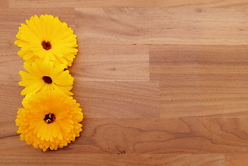 Image showing Three yellow calendula flowers on wooden background